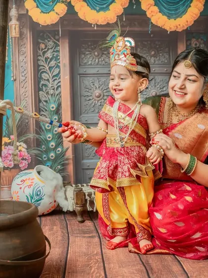 A wide shot capturing the joy of both mother and child within the full Janmashtami setup.