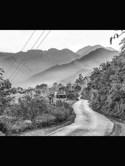 A winding road disappears into the misty mountains, with a lone bus making its journey. This black and white photograph, titled 'Journey', evokes a sense of travel and the path ahead, a narrative landscape print for any collection.