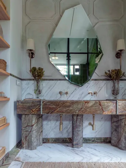 A detail of the master bathroom in Summer Haus, showcasing our passion for material expression. Here, a custom-fabricated vanity from richly veined marble stands as a sculptural element, complemented by a uniquely shaped mirror and artisanal wall sconces.