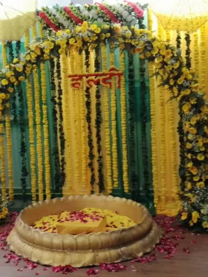 A classic Haldi ceremony setup with a floral arch and a large brass urli. The backdrop of green and yellow marigold strings is perfect for creating a classic and auspicious atmosphere.