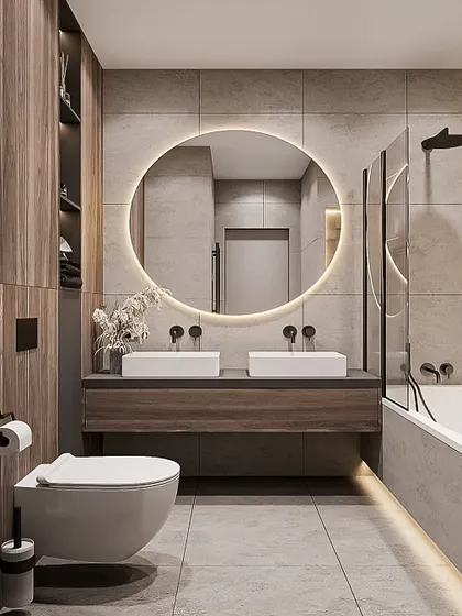 This bathroom features a large, round back-lit mirror as its centerpiece. The floating wood vanity and grey tiles create a contemporary and calming space.