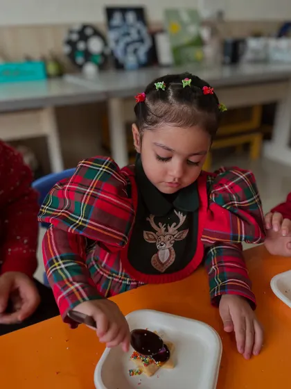 A child carefully decorates a cookie with chocolate, a delicious and creative activity from our holiday workshop.