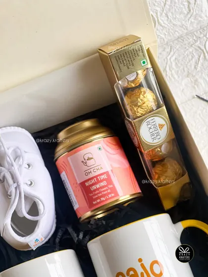 A classic combination of Ferrero Rocher chocolates, herbal tea, and baby's first shoes makes for an elegant and sweet announcement gift.