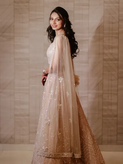 An elegant full-length portrait of the bride, showing off her beautiful lehenga and the sheer cape.