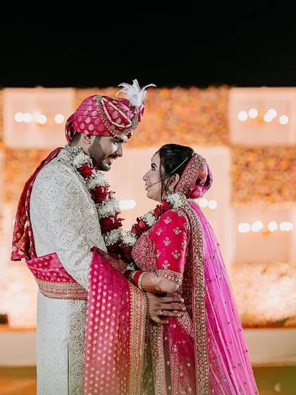 A candid moment during the Varmala ceremony, with the couple sharing a look of love in front of their beautiful floral and chandelier stage.