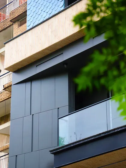 A detail shot showing the contrast between the dark grooved panels, the wood-finish balcony, and the textured shingles. This interplay of materials adds depth and character to the facade.