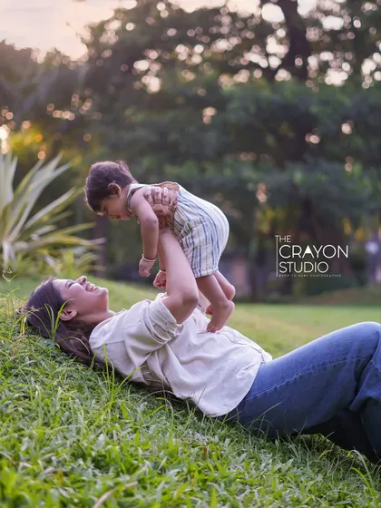 A mother's love, captured in a moment of play. Lying in the soft grass, she lifts her baby up, their smiles reflecting the pure joy of their connection during a sunny afternoon family session.