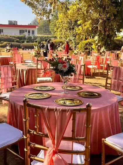 An overview of the outdoor dining area, featuring tables dressed in pastel pink linens with matching chair drapes and elegant gold chiavari chairs.