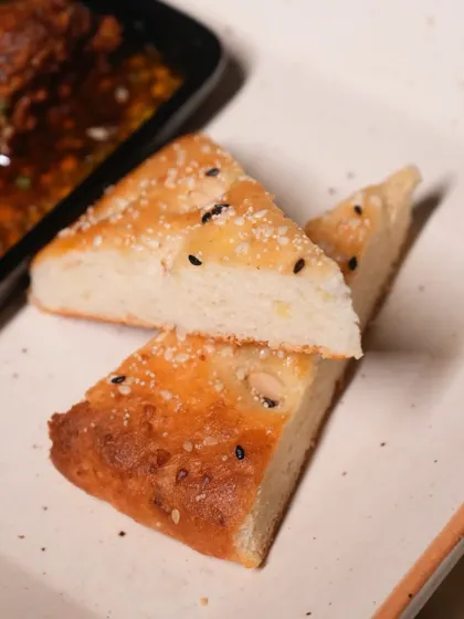 A close-up of our house-made bread, soft and fluffy with a sprinkle of nigella seeds. It's the perfect vessel for our sizzling mutton seekh.