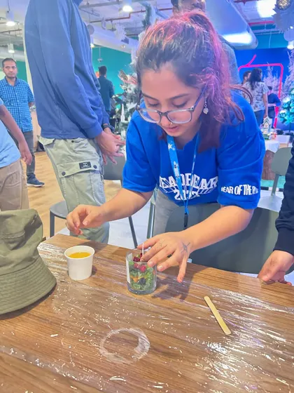 A participant carefully places small red wax embeds into her candle during a Christmas-themed workshop, demonstrating the detailed, hands-on nature of the activity.