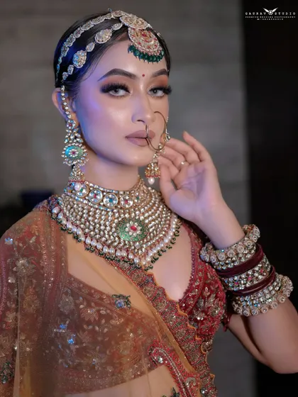 A close-up portrait focusing on the bride's stunning, heavy jewellery. The pose, with her hand near her face, draws attention to the large earrings and her flawless makeup.