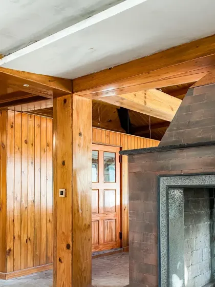 An interior shot during construction, highlighting the use of natural pine wood paneling and a rustic stone fireplace, materials chosen to reflect the local environment.