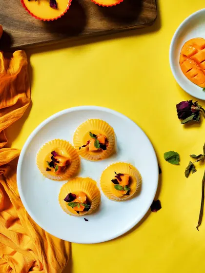 A flatlay of bright yellow mango pudding tarts on a white plate. The vibrant yellow background and scattered petals create a cheerful, summery vibe that's full of energy.