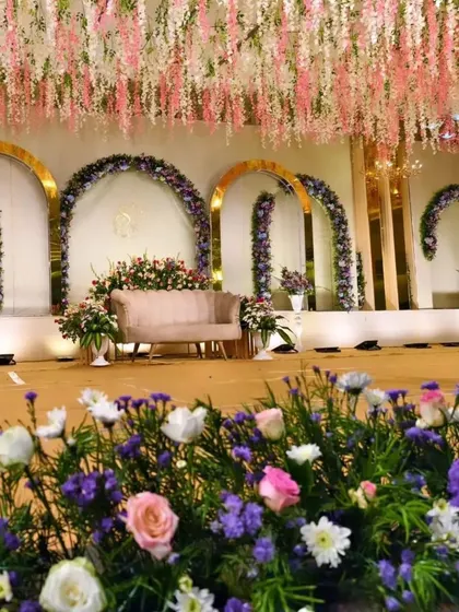 A premium reception stage with a ceiling of hanging pink and white wisteria. The golden arches and purple floral arrangements add to the luxurious and dreamy feel.