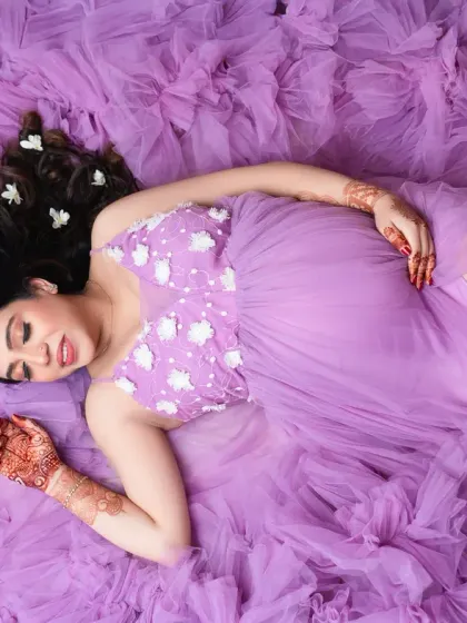 Dreaming of you. This overhead shot captures the mother-to-be lying on a bed of purple tulle, her hair adorned with flowers. It's a romantic and artistic perspective.