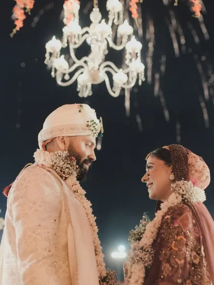 A close-up of Nidhi and Alok during their varmala, their eyes locked in a moment of pure love and connection under the grand chandelier.