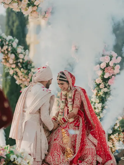 A romantic Varmala moment, with the couple looking into each other's eyes, enveloped in a gentle cloud of smoke under a floral arch.