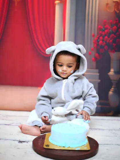 The aftermath of a fun cake smash! This baby, dressed in a cute animal onesie, is enjoying the mess he made with his blue birthday cake.
