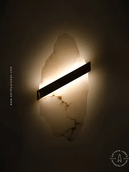 This artistic wall sconce features a raw, organically shaped slab of translucent marble. A simple diagonal metal bar houses the light, which glows through the stone to reveal its natural veining and character.