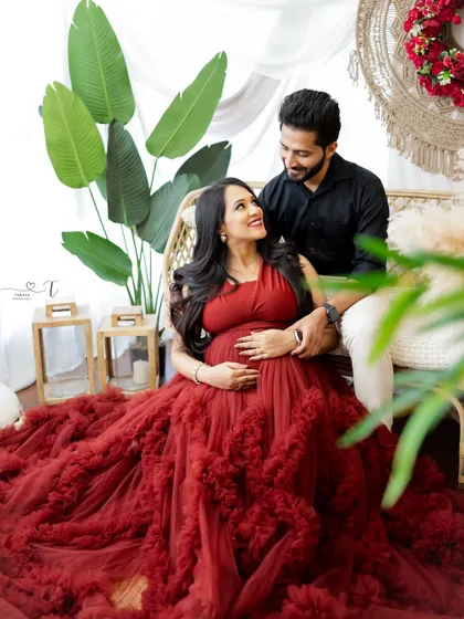 A candid moment of love and laughter in a boho-inspired setting. The rich red of the gown contrasts beautifully with the natural textures of the studio decor.