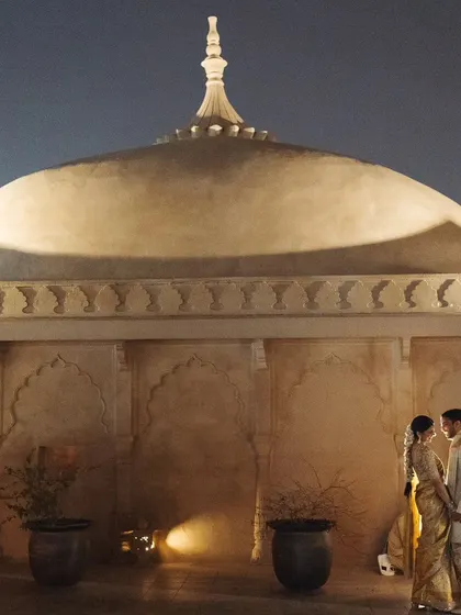 A romantic portrait of the couple against the illuminated dome of a palace at night, capturing a moment of quiet elegance during their wedding celebrations.