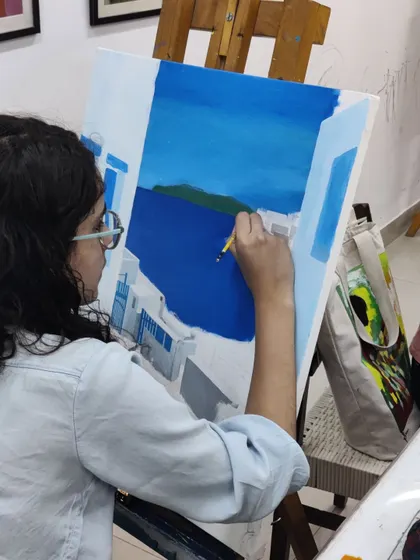 A focused shot of the student adding subtle shading and highlights to the white walls, giving them form and dimension in her Santorini landscape.