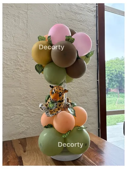 A jungle-themed balloon centerpiece with a small plush leopard, using a palette of green, brown, and pink.