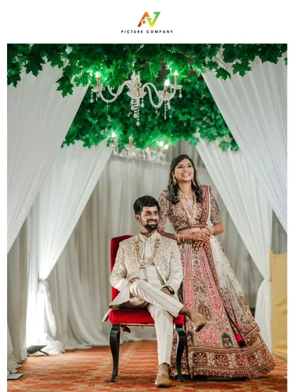 A regal reception portrait, with the groom seated and the bride standing elegantly by his side.
