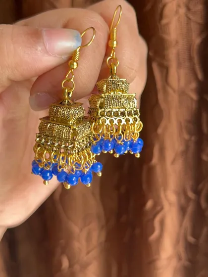 A pair of three-tiered gold-oxidised jhumkas with blue beads. These are lightweight and affordable, making them great for daily or college wear.