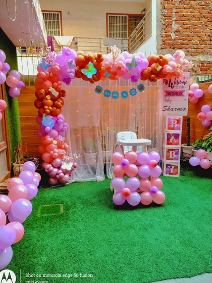 An outdoor welcome party for a baby, with a balloon arch and "BABY" blocks set up on an artificial grass lawn.