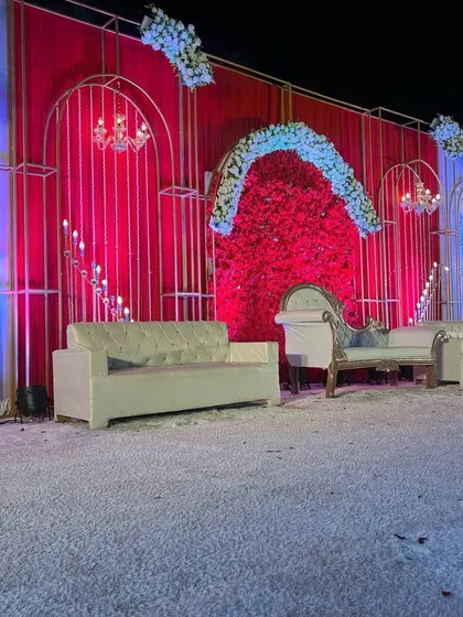 A wider view of the opulent all-red wedding stage. The combination of red drapes, a red flower wall, and white floral arches creates a multi-dimensional and luxurious look.