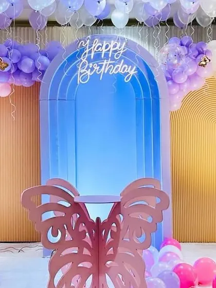 An elegant butterfly birthday setup featuring a blue lighted arch backdrop. The decor is accented with pastel purple and pink balloons and a delicate butterfly prop, perfect for a sophisticated celebration.