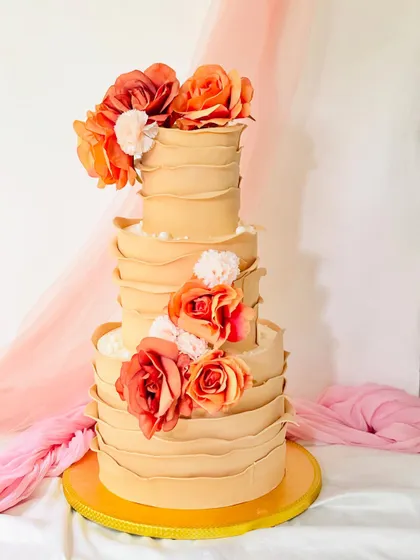 A grand three-tiered cake with a unique ruffled buttercream texture in a warm beige tone. It's decorated with clusters of vibrant orange and red sugar flowers, making a bold statement.
