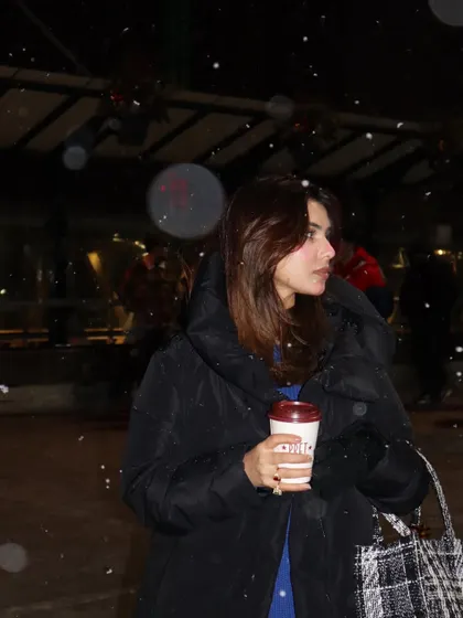 A close-up in the snow, holding a coffee and wearing the Mango and Vero Moda winter outfit.