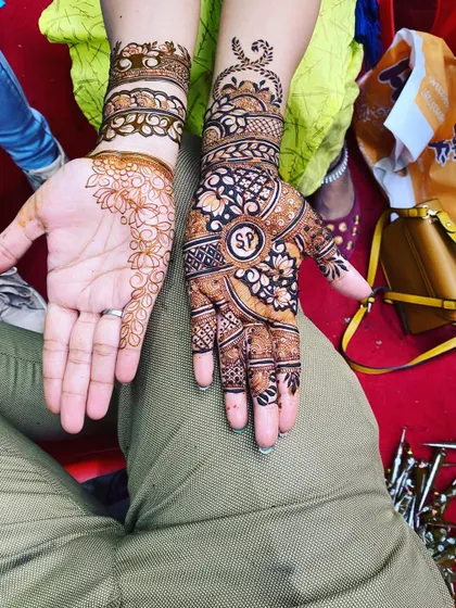 A great example of guest mehendi. One hand has a simple floral bail, while the other has a more detailed design with a personalized initial 'SP' in the center.