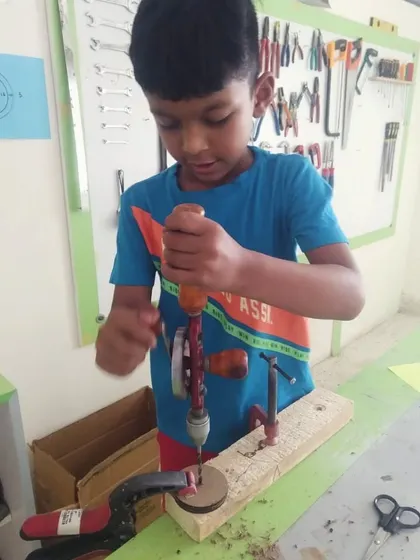 A student uses a hand drill to make a precise hole in a wooden block. This activity builds focus and fine motor skills.