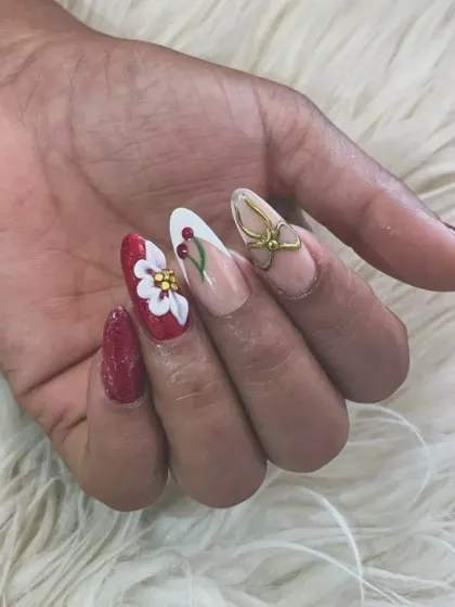 A festive and artistic 3D nail set. This design features a bold red base, a hand-sculpted white flower, painted holly leaves, and a stunning 3D gold bow accent nail.