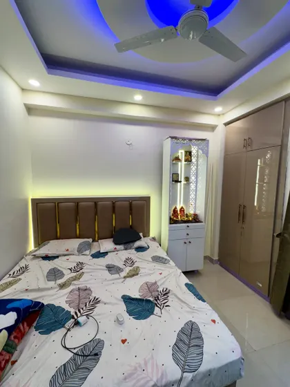 This bedroom design cleverly incorporates a compact mandir unit. The false ceiling has both white and blue LED lighting options to change the mood.