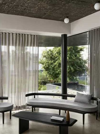 Inside Pavilion House, the living area is defined by soft grey tones, a textured ceiling, and floor-to-ceiling curtains that filter the natural light. The minimalist furniture and open plan create a sense of calm and spaciousness, with the focus always drawn to the views outside.