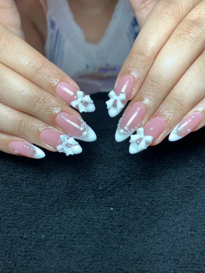 A classic French manicure gets an upgrade with 3D sculpted bows. This elegant design features white tips on almond-shaped nails, accented with delicate bows and pearls for a bridal or special occasion look.