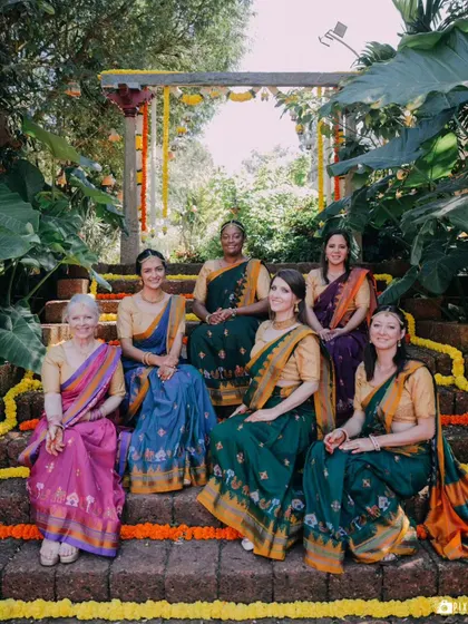 The bride's side, beautifully dressed in traditional sarees, posing on the decorated steps of The Peacock Grove.