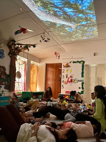 Inspired by a visit to Scandinavia, we began experimenting with projectors in our classrooms. Here, the children lie on the floor, mesmerized by images of a forest canopy projected onto the ceiling, transforming the room into a magical world.