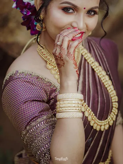 A shy, happy smile from a beautiful Hindu bride, her hand gently touching her face, showcasing her intricate henna and traditional jewelry.
