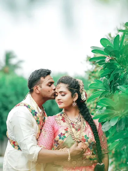 A tender moment captured in a garden setting, with the groom placing a gentle kiss on the bride's forehead.