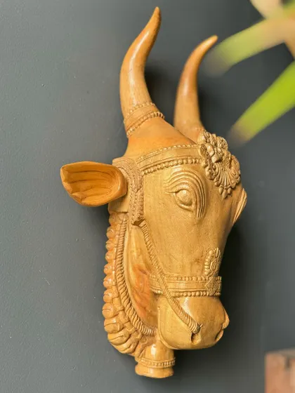 A beautifully detailed, hand-carved wooden bull head. The natural wood grain and intricate ornamentation make this a sophisticated piece of wall art that connects with Indian cultural traditions.