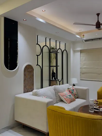 A cozy 2BHK living room with bright yellow accent chairs that add a pop of color. A stylish partition with shelves provides separation without closing off the space.