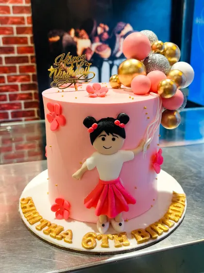 A charming pink cake with a fondant girl figurine holding a bouquet of balloons for a 6th birthday.
