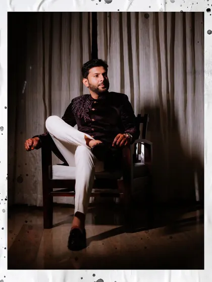 A dapper, full-length portrait of the groom seated, showcasing his modern-traditional Sangeet outfit.