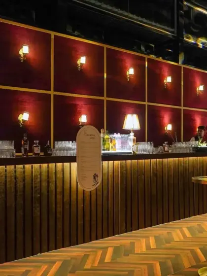 A closer look at the speakeasy bar. The design features a warm, vertically lit wooden base, a velvet-paneled back wall, and soft lamp lighting to create an inviting, old-world ambiance.
