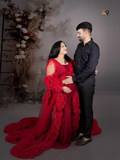 A loving gaze between partners. This shot captures the couple's connection, with the mom-to-be looking radiant in a red gown against a beautifully textured, rustic floral backdrop.